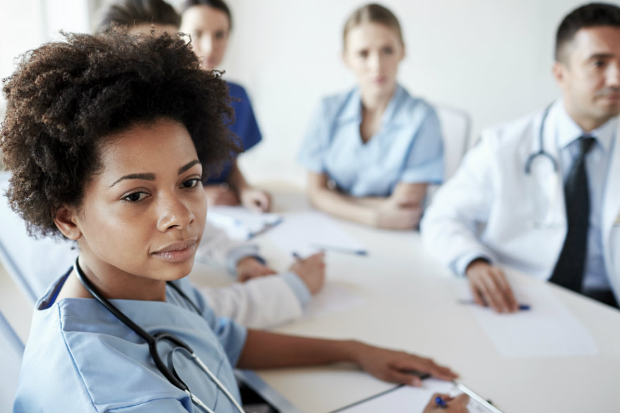 A woman in scrubs sitting in a meeting with other nurses.