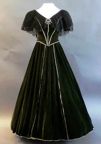 The gown on a dress form. Green velvet with a full bottom and white satin piping the skirt and seams