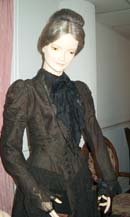 A long-sleeved black lace over black taffeta dress is shown on a mannequin from the waist up.