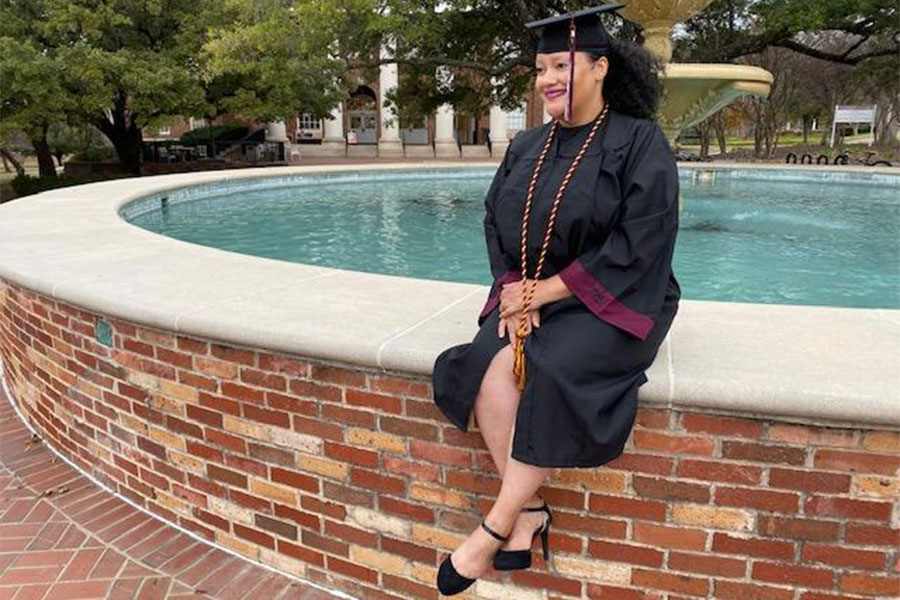 Cheryl Brown sits by the fountain on TWU's Denton campus in her graduation gown.