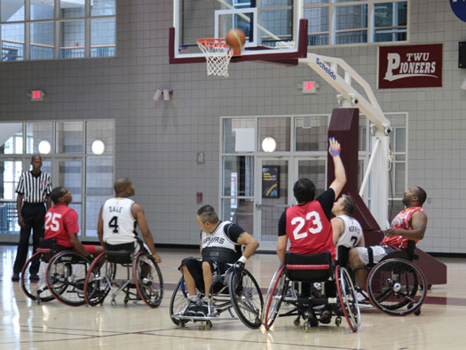 A group of people in wheelchairs play basketball together