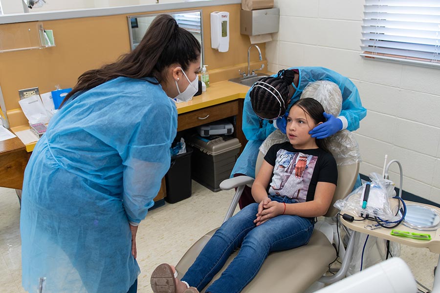 a student examines a child's mouth while another student looks on in a dental hygiene clinic