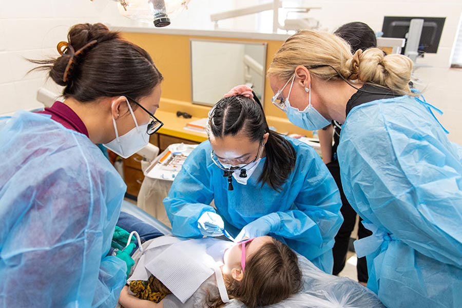 a dental hygienist student examines a child's mouth while staff members look on