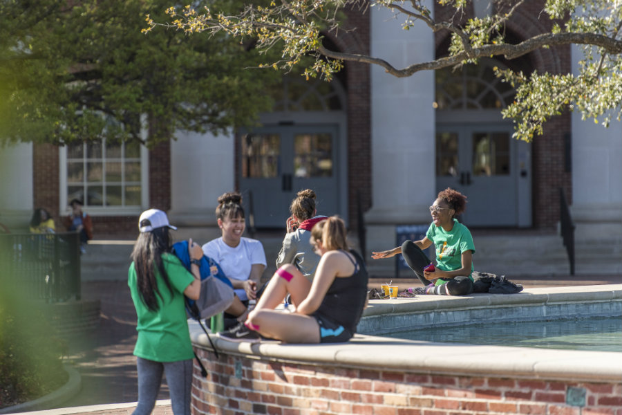 A group of students on a sunny day sitting around the fountain on TWU's Denton campus.