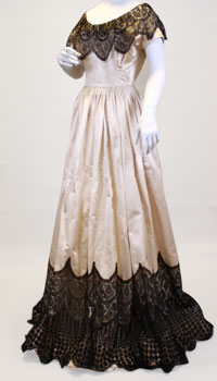 A heavy ivory satin dress with black Spanish lace trim circling the skirt and shoulders.