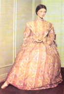Dress made of sheer muslin with a full skirt, high neckline, double bell sleeves, and fitted bodice.