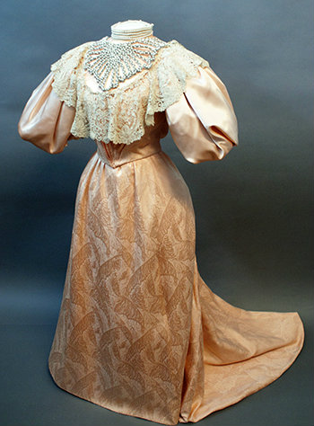 The full gown is shown on a dress form. It is a light salmon taffeta brocade with a lace collar. 