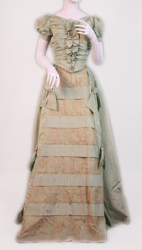 The dress is made of turquoise moiré taffeta trimmed with bows and has lace inserts on front panel. 
