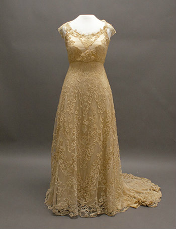 The full gown is shown on a dress form. It is a gold lace with cap sleeves.