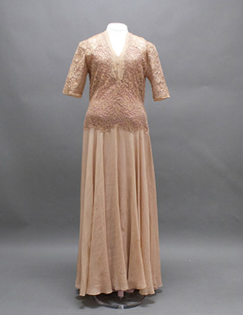 A cream colored dress with a V-neck and mid-length sleeves. The bodice is covered in a cream lace.