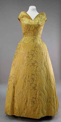 A long, gold brocade dress is shown on a dress form. It has cap sleeves and a natural waistline.