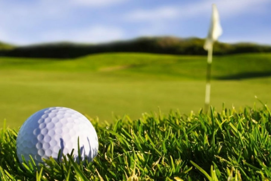 A close-up photo of a golf ball with the view of a golf course behind it.