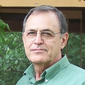 A photo of a man with glasses and wearing a green collared shirt.